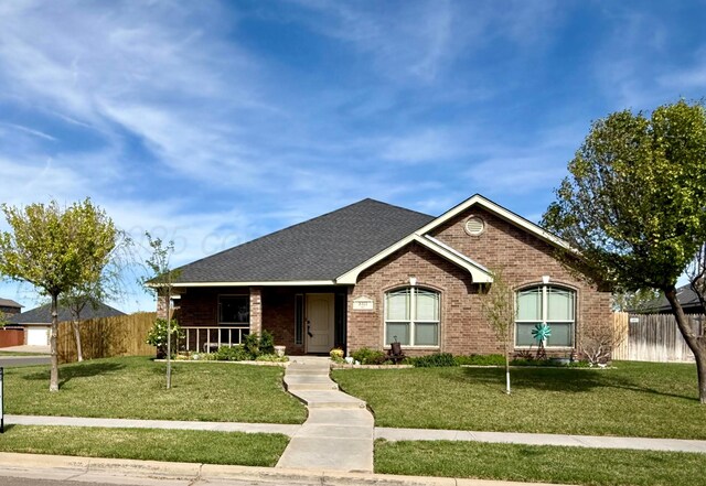 single story home with fence, roof with shingles, covered porch, brick siding, and a front yard