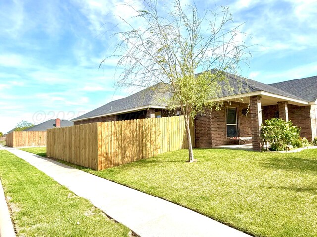 view of front of home featuring brick siding, roof with shingles, a front yard, and fence