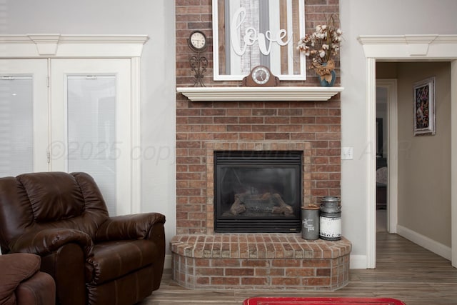 living area featuring baseboards, a brick fireplace, and wood finished floors
