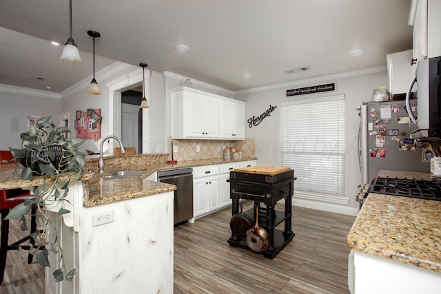 kitchen featuring a sink, decorative backsplash, appliances with stainless steel finishes, a peninsula, and ornamental molding