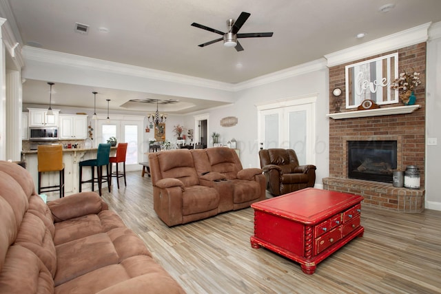 living area with a ceiling fan, a brick fireplace, crown molding, and light wood-style flooring