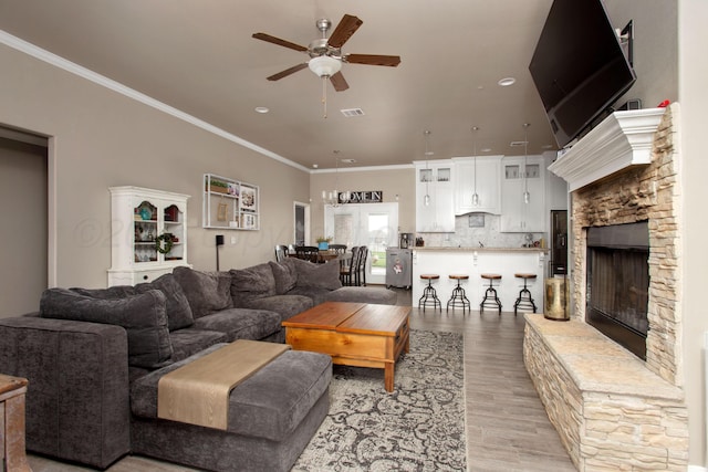 living room with ceiling fan, light hardwood / wood-style floors, crown molding, and a stone fireplace