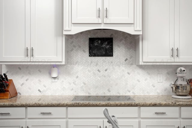 kitchen featuring white cabinets, black electric cooktop, backsplash, and light stone countertops