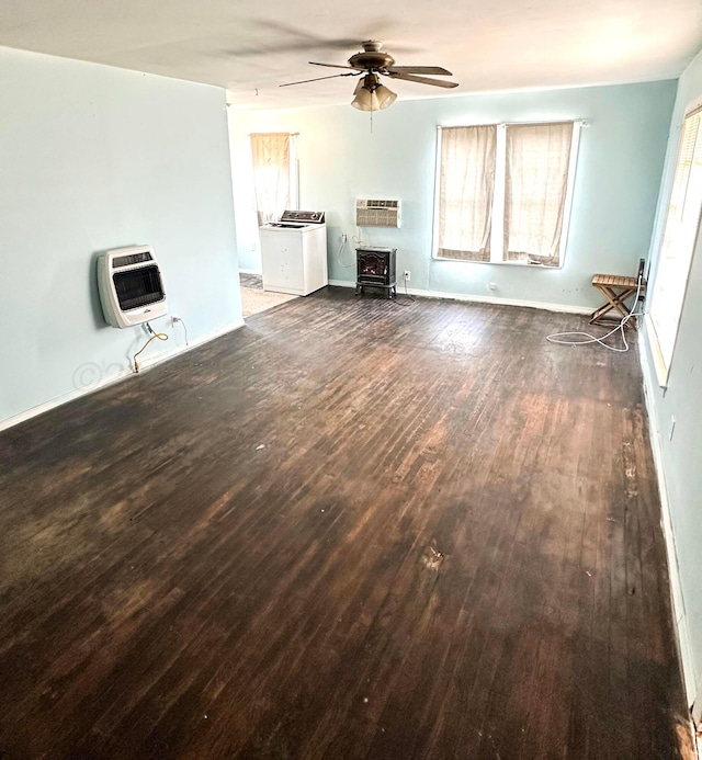 unfurnished living room with heating unit, a wood stove, dark hardwood / wood-style flooring, ceiling fan, and washer / clothes dryer