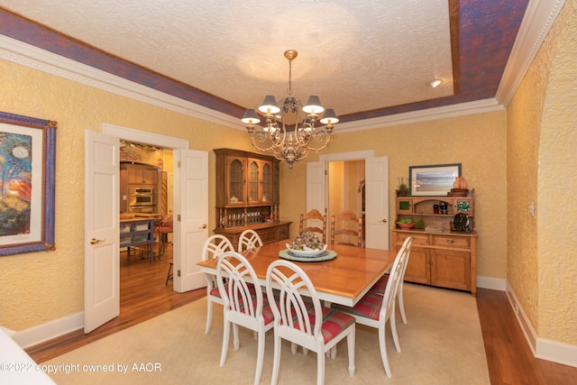 dining area with light wood-type flooring, an inviting chandelier, ornamental molding, and a textured ceiling