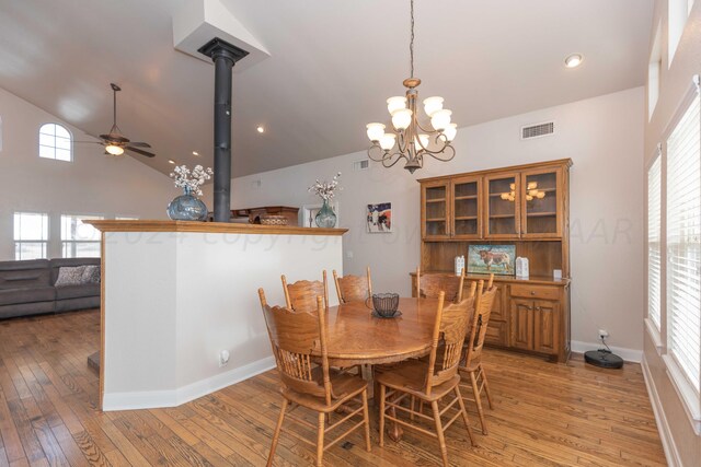 dining space with light wood-type flooring, lofted ceiling, a wood stove, and plenty of natural light