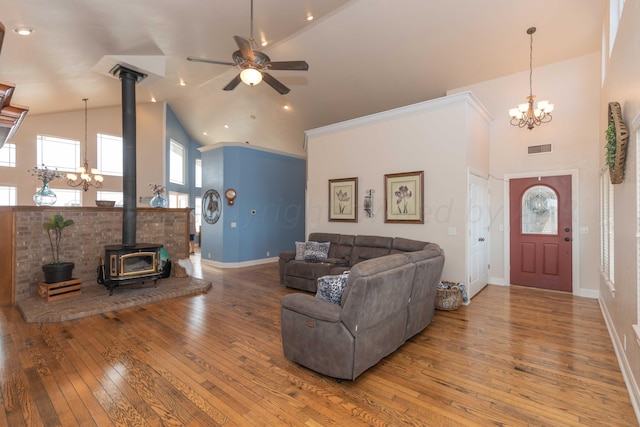 living room with hardwood / wood-style floors, ceiling fan with notable chandelier, a wood stove, and high vaulted ceiling