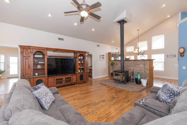 living room featuring light hardwood / wood-style floors, ceiling fan with notable chandelier, a wood stove, and high vaulted ceiling