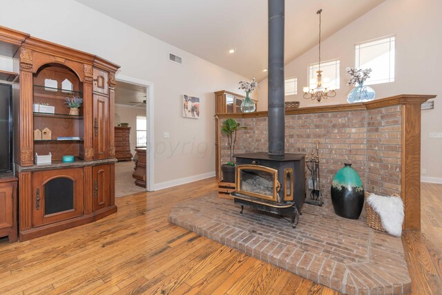 living room featuring a notable chandelier, a wood stove, high vaulted ceiling, and light hardwood / wood-style flooring