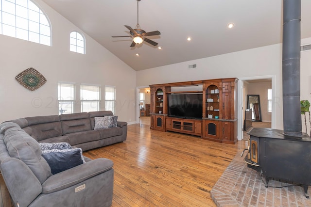 living room featuring hardwood / wood-style floors, ceiling fan, a wood stove, and high vaulted ceiling