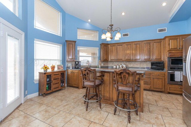 kitchen with stainless steel appliances, decorative light fixtures, light tile patterned floors, decorative backsplash, and a breakfast bar