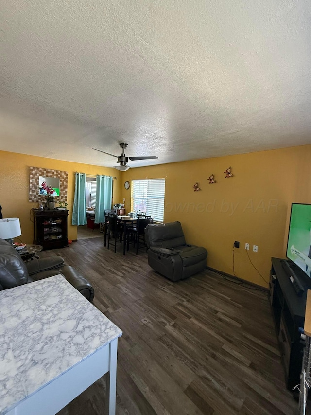 living room with a textured ceiling, ceiling fan, and dark wood-style flooring