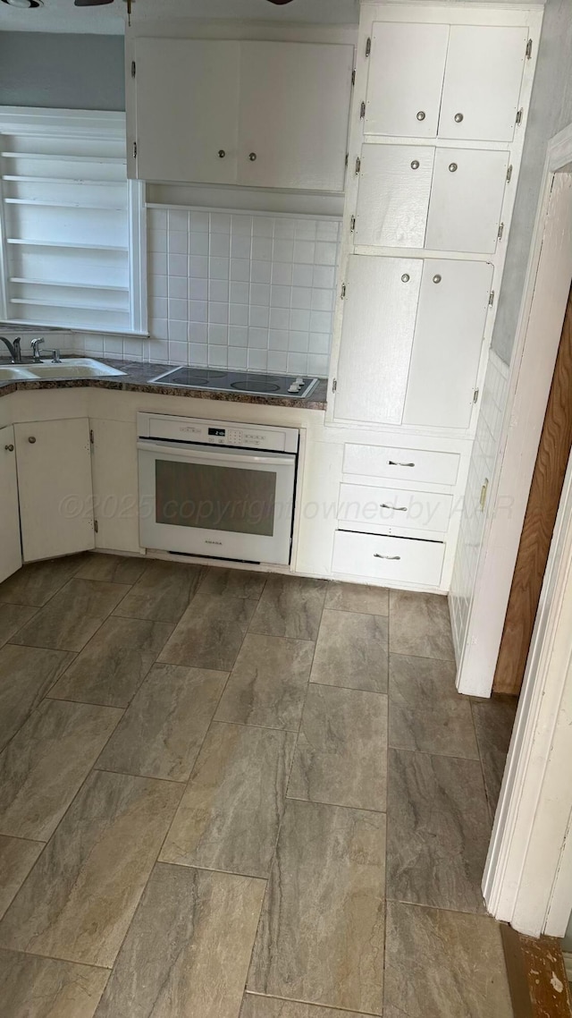 kitchen with stone finish floor, white cabinetry, decorative backsplash, a sink, and oven