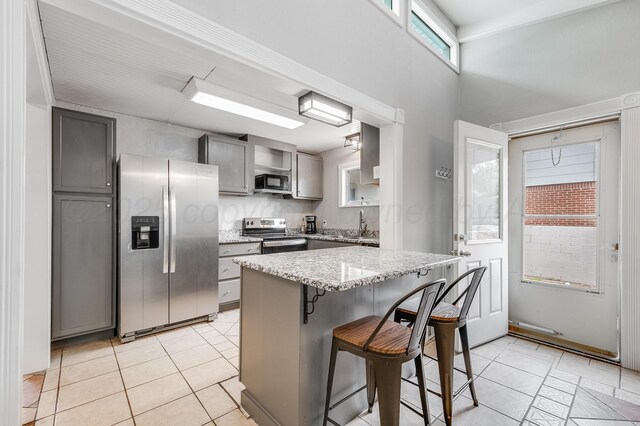 123 Bellaire Ave, Dumas, TX 79029 - kitchen with stainless steel appliances, gray cabinets, a kitchen bar, light tile patterned floors, and light stone countertops