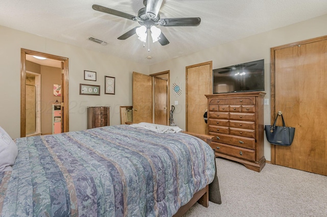 bedroom with ceiling fan, a textured ceiling, carpet flooring, visible vents, and two closets