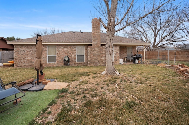 back of property with a yard, a chimney, fence, and brick siding