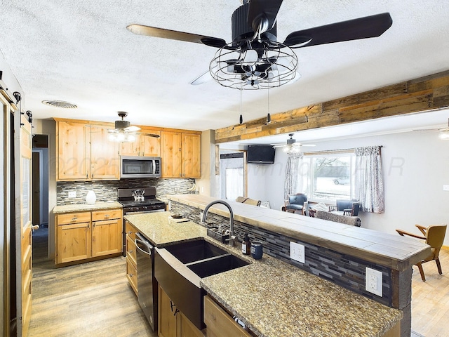 kitchen featuring ceiling fan, appliances with stainless steel finishes, a barn door, and backsplash