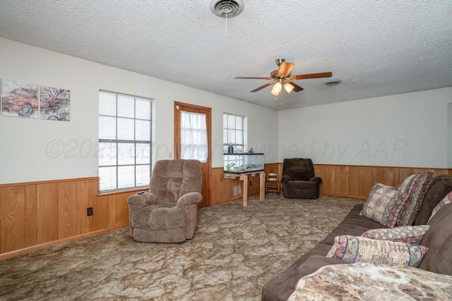 carpeted living room with visible vents, a textured ceiling, wooden walls, and wainscoting