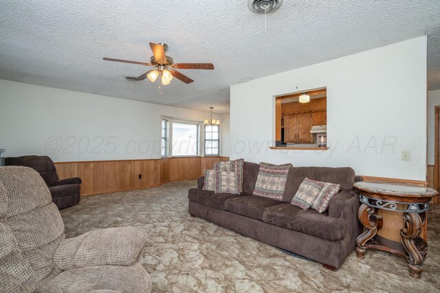living room featuring a wainscoted wall, a textured ceiling, wood walls, carpet, and ceiling fan with notable chandelier