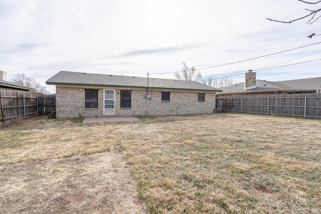 rear view of property with brick siding, a fenced backyard, a yard, and a patio area