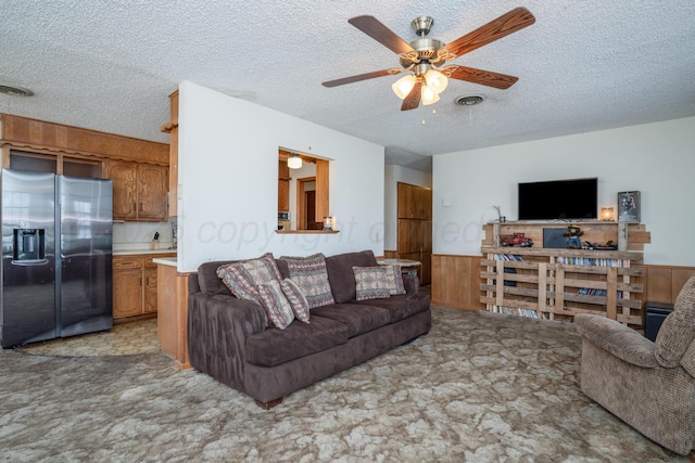 living area featuring a textured ceiling, visible vents, a ceiling fan, wainscoting, and light colored carpet