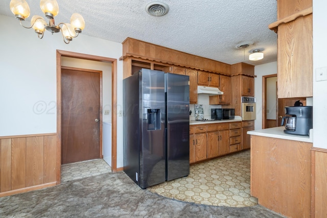 kitchen featuring light countertops, a chandelier, appliances with stainless steel finishes, under cabinet range hood, and wainscoting