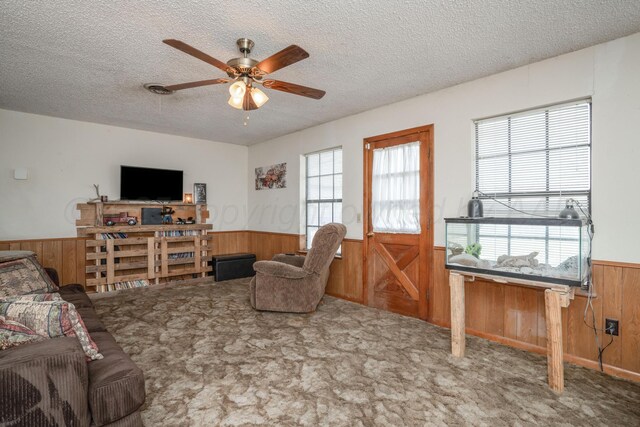 carpeted living room featuring a wainscoted wall, wooden walls, ceiling fan, and a textured ceiling