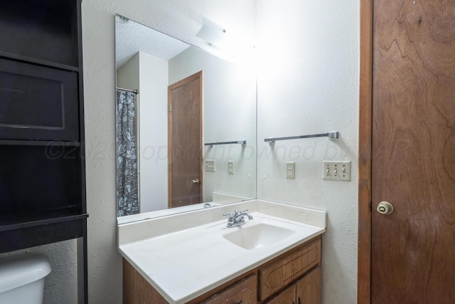 full bath featuring toilet, vanity, and a textured wall