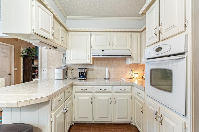 5216 Westway Trl, Amarillo, TX 79109 - kitchen featuring white oven, a peninsula, under cabinet range hood, tasteful backsplash, and ornamental molding