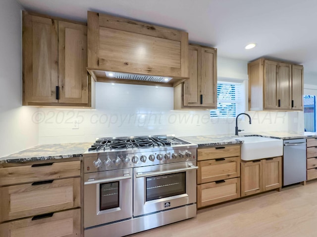 kitchen with light brown cabinets, appliances with stainless steel finishes, a sink, and light stone counters