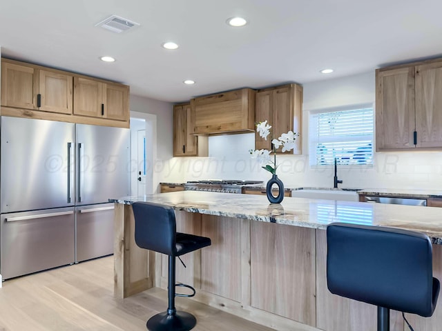 kitchen featuring visible vents, a kitchen breakfast bar, light stone countertops, stainless steel appliances, and premium range hood