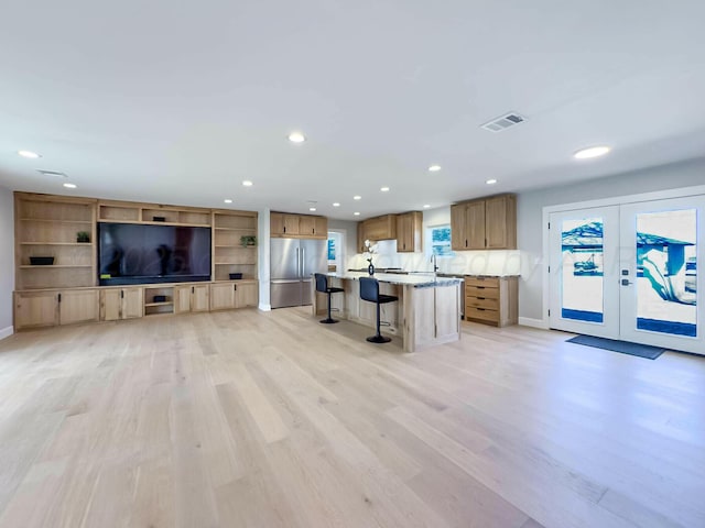 kitchen with a breakfast bar, light wood-style flooring, visible vents, and stainless steel refrigerator