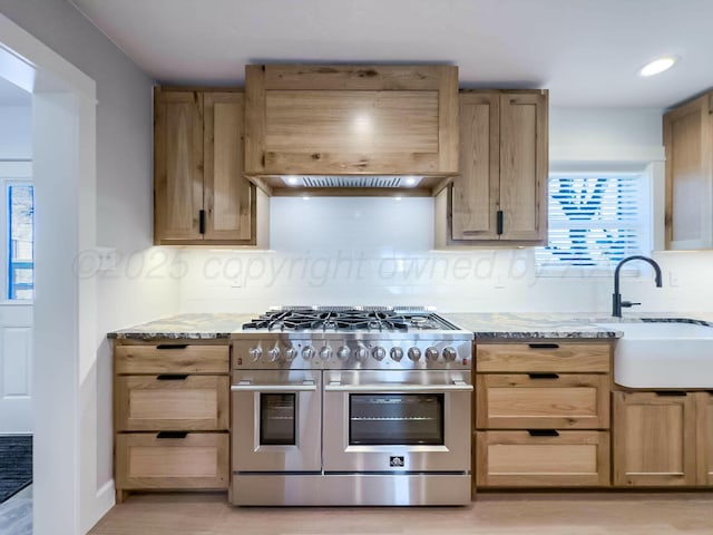 kitchen with light stone counters, double oven range, a sink, and backsplash