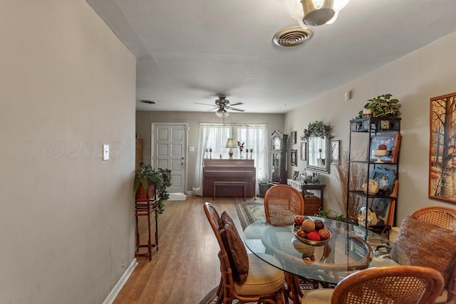 dining area with light wood-style flooring, a ceiling fan, visible vents, and baseboards