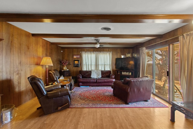 living room with visible vents, beamed ceiling, wood walls, and wood finished floors