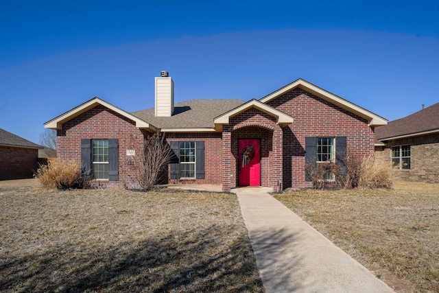 single story home with roof with shingles, brick siding, a chimney, and a front lawn