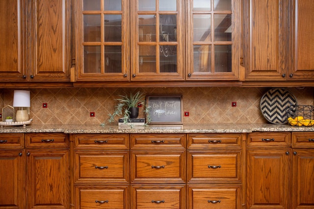 4602 Cape Verde Ct, Amarillo, TX 79119 - kitchen with light stone countertops, glass insert cabinets, backsplash, and brown cabinetry