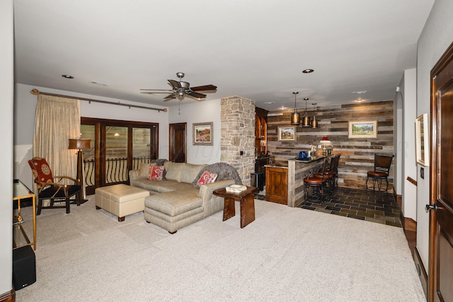 carpeted living room with indoor bar, ceiling fan, and wood walls