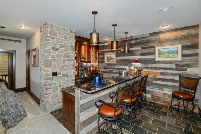 bar featuring pendant lighting, black dishwasher, dark stone countertops, and wood walls