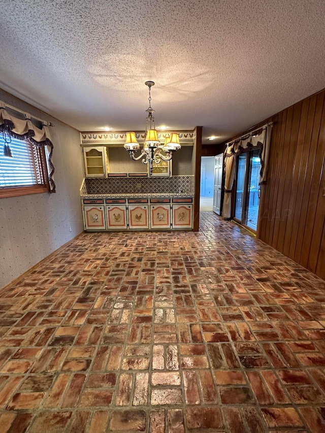 unfurnished dining area featuring a textured ceiling, wooden walls, and an inviting chandelier