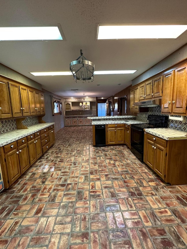 kitchen with backsplash, black appliances, kitchen peninsula, and a notable chandelier