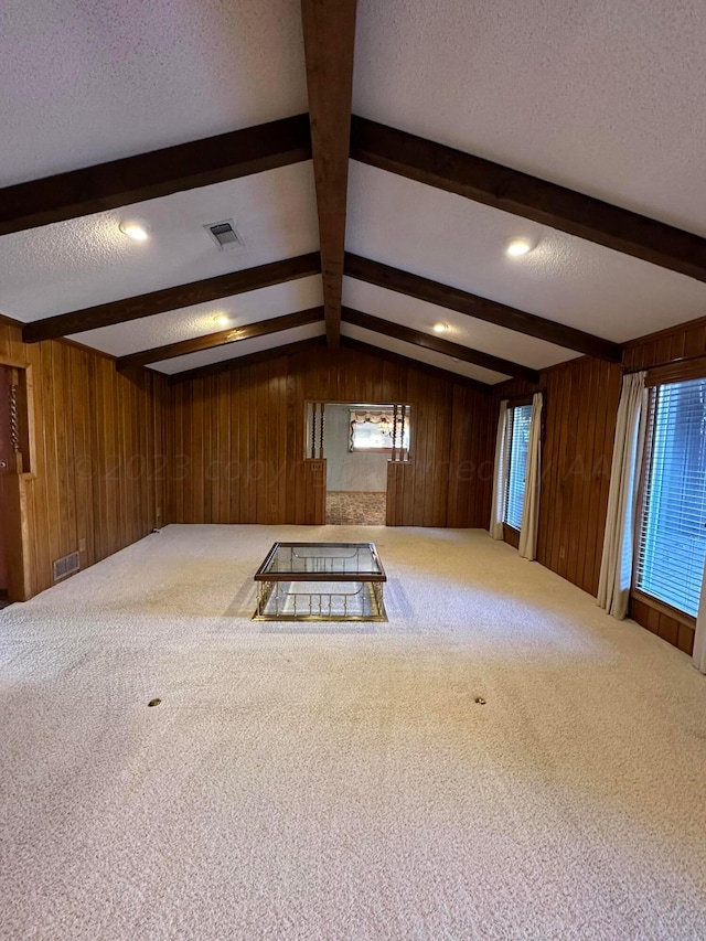 carpeted empty room with lofted ceiling with beams, wooden walls, and a textured ceiling