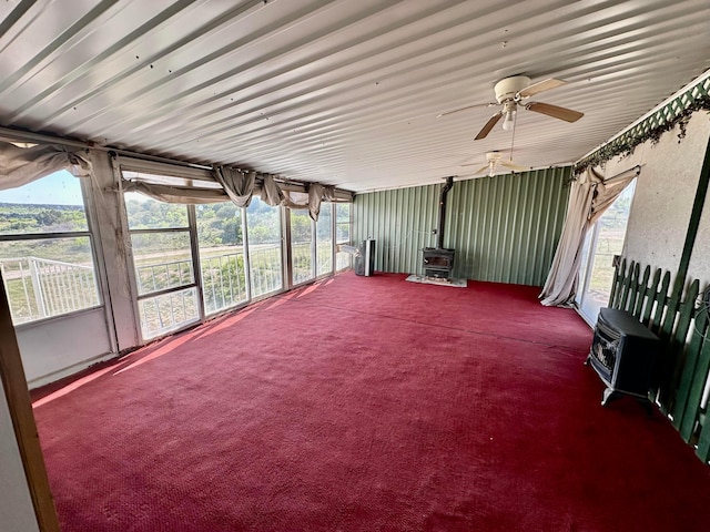 unfurnished sunroom featuring ceiling fan, heating unit, and a wood stove