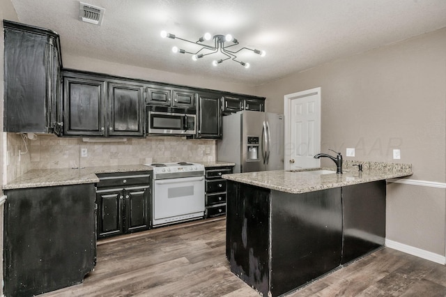 kitchen featuring appliances with stainless steel finishes, dark cabinets, a sink, dark wood finished floors, and a chandelier