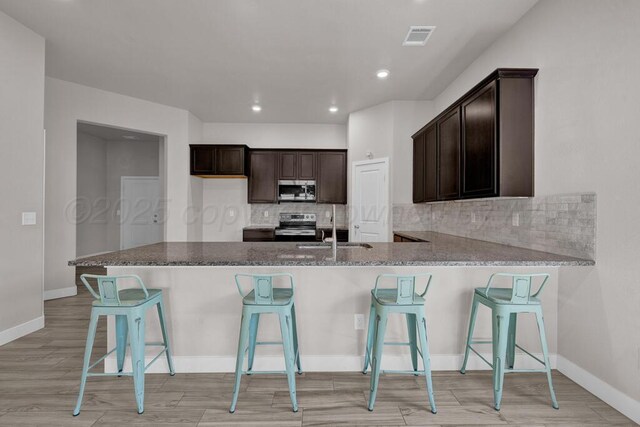9110 Lexford Dr, Amarillo, TX 79119 - kitchen with stainless steel appliances, light wood-style floors, dark brown cabinetry, decorative backsplash, and recessed lighting