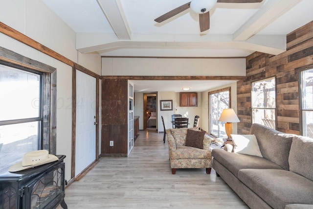 living room featuring light wood-type flooring, wooden walls, a healthy amount of sunlight, and beam ceiling