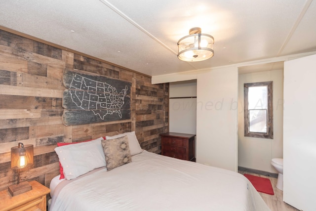 bedroom featuring a textured ceiling, wood-type flooring, wooden walls, and connected bathroom