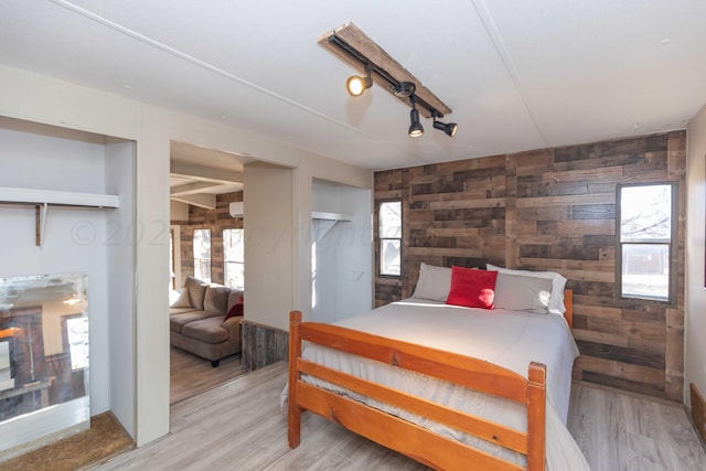 bedroom featuring light hardwood / wood-style flooring, wooden walls, and multiple windows