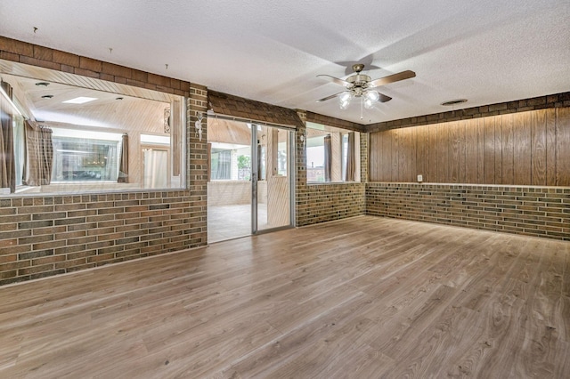 613 Bennett Dr, Dumas, TX 79029 - empty room featuring brick wall, wood finished floors, ceiling fan, wooden walls, and a textured ceiling