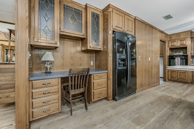 613 Bennett Dr, Dumas, TX 79029 - kitchen with black appliances, light wood-type flooring, crown molding, wood walls, and brown cabinetry